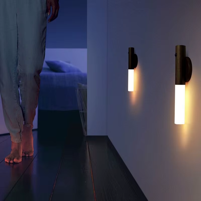 Person walking barefoot in a dark hallway at night with two wooden LED motion sensor wall lights glowing in warm white