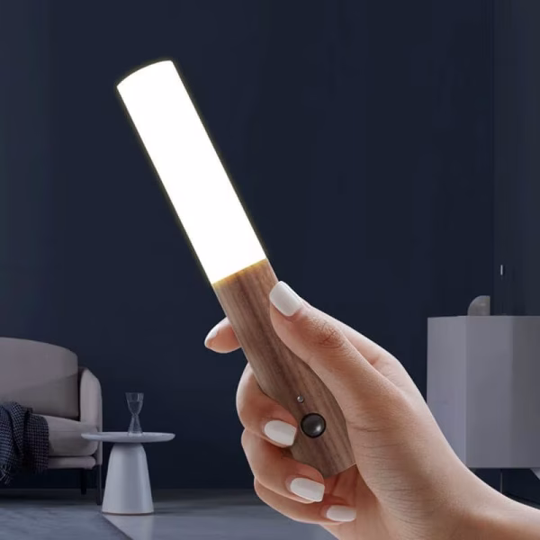 Hand holding a detached wooden LED night light with bright white glow, usable as a portable flashlight or rechargeable torch
