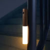 Wooden motion sensor night light mounted vertically on a staircase railing, glowing with warm white light in a dark stairwell