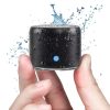 A pair of hands holding a small black waterproof Bluetooth speaker with water splashing around it